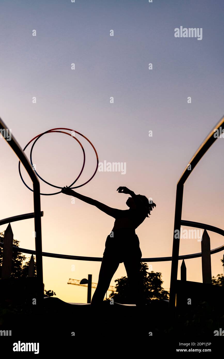 Silhouette sportive femme s'exerçant avec des cerceaux en plastique contre le ciel clair au coucher du soleil Banque D'Images