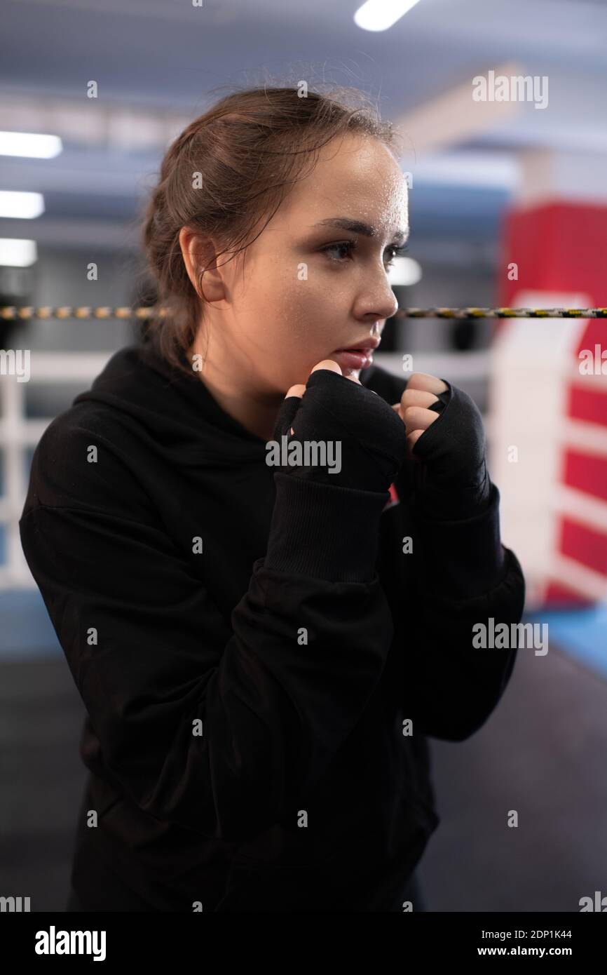 Déterminé femme combattant pratiquant une posture de protection pendant la boxe à l'ombre anneau pendant l'entraînement dans la salle de gym Banque D'Images