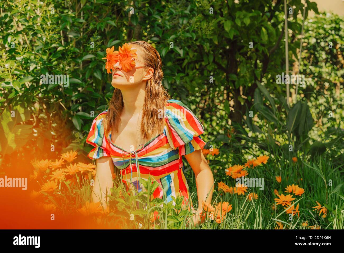 Femme dans la nature portant des lunettes avec des fleurs d'orange qui la couvrent yeux Banque D'Images