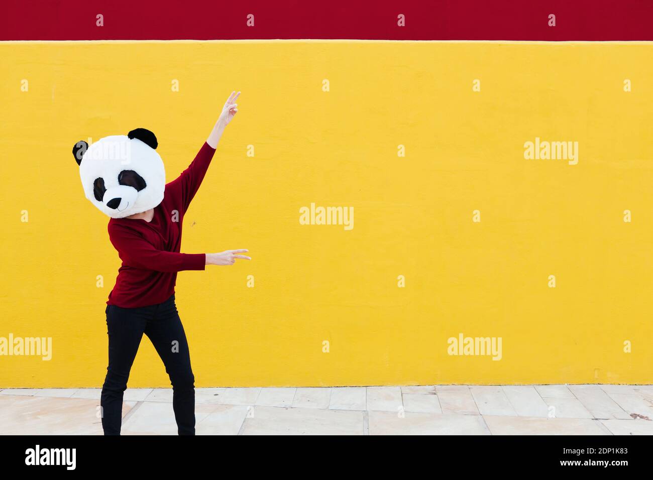 Femme portant un masque de panda tout en dansant contre le mur jaune Banque D'Images