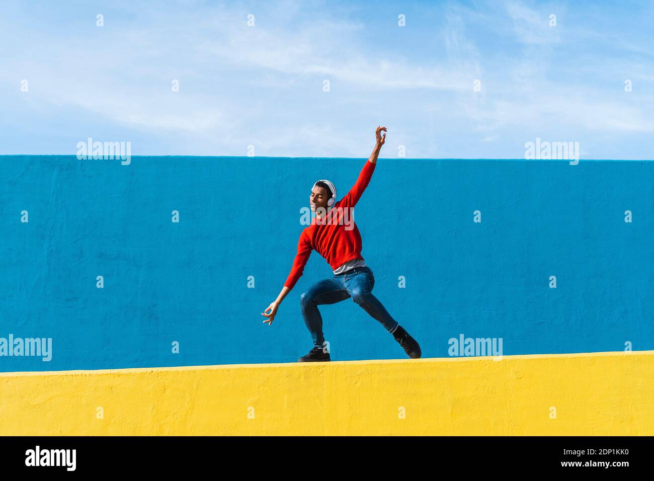 Jeune homme avec des écouteurs, l'écoute de la musique, de la danse sur le mur jaune Banque D'Images
