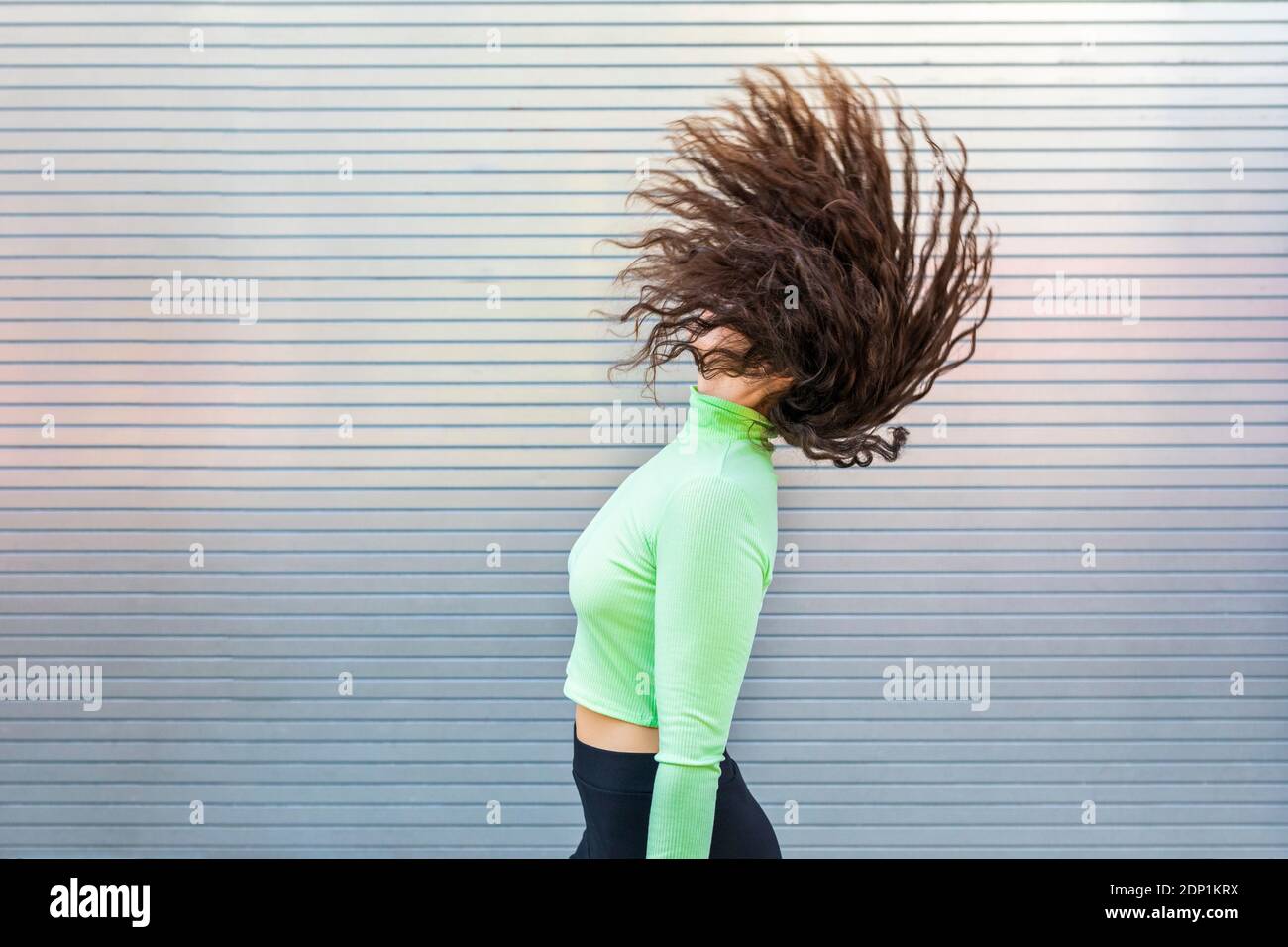 Une jeune femme se lance sur les cheveux tout en se tenant debout près d'un mur gris Banque D'Images Une jeune femme se lance sur les cheveux tout en se tenant debout près d'un mur gris Banque D'Images
