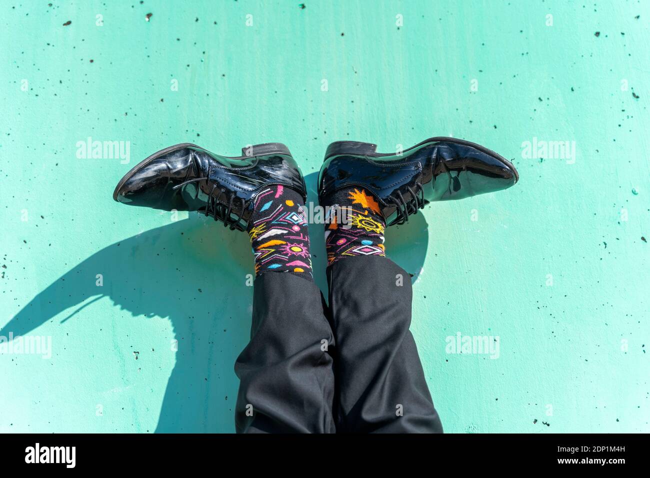 Pieds d'homme d'affaires portant des chaussettes colorées contre un mur vert Banque D'Images