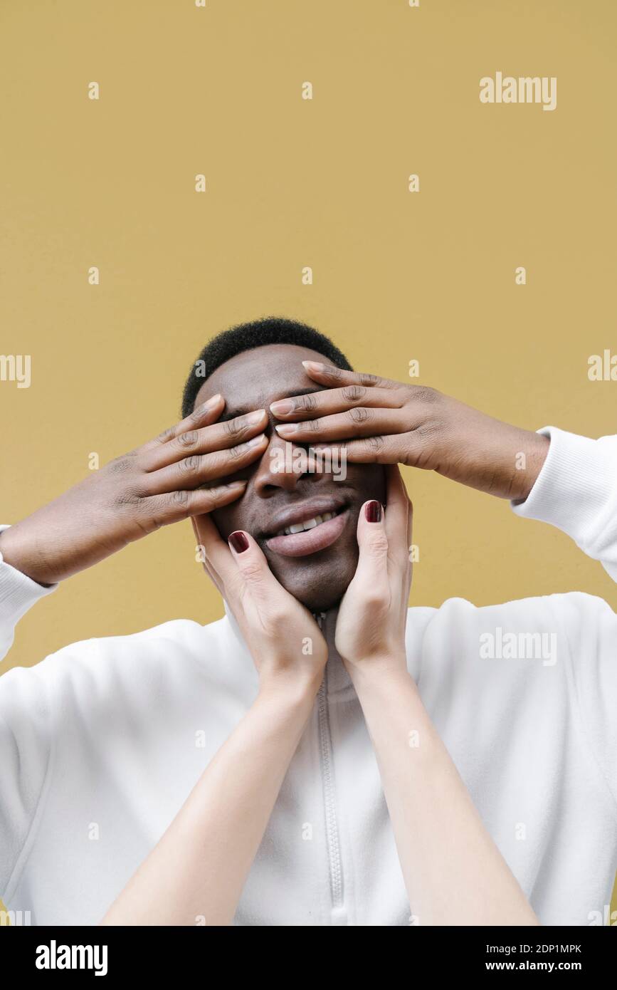 Portrait d'un homme souriant couvrant les yeux avec ses mains, touché par les mains de la femme Banque D'Images