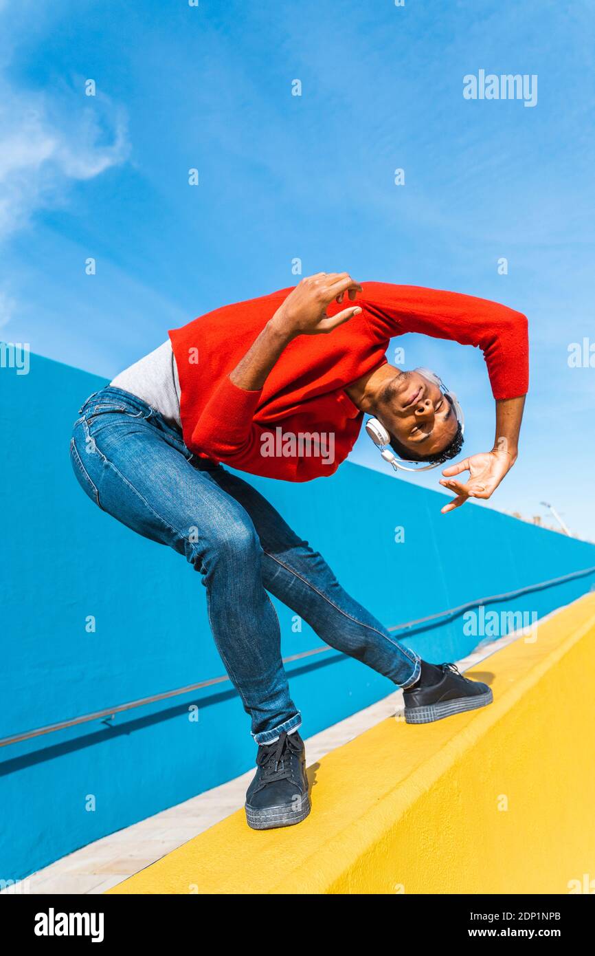 Jeune homme avec des écouteurs, l'écoute de la musique, de la danse sur le mur jaune Banque D'Images