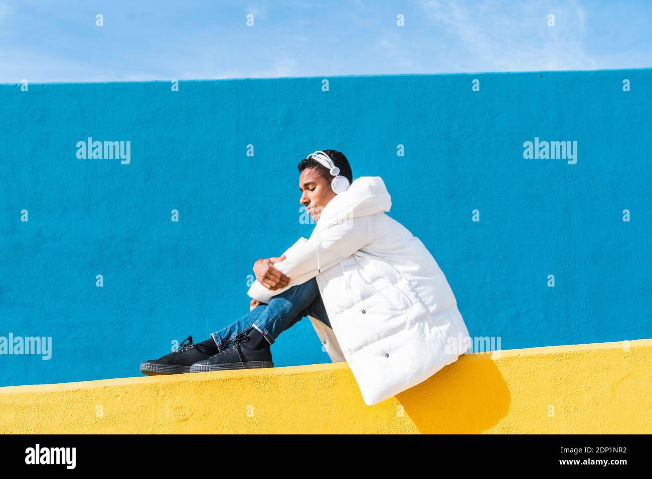 La mode jeune homme assis sur le mur jaune, écouter de la musique Banque D'Images