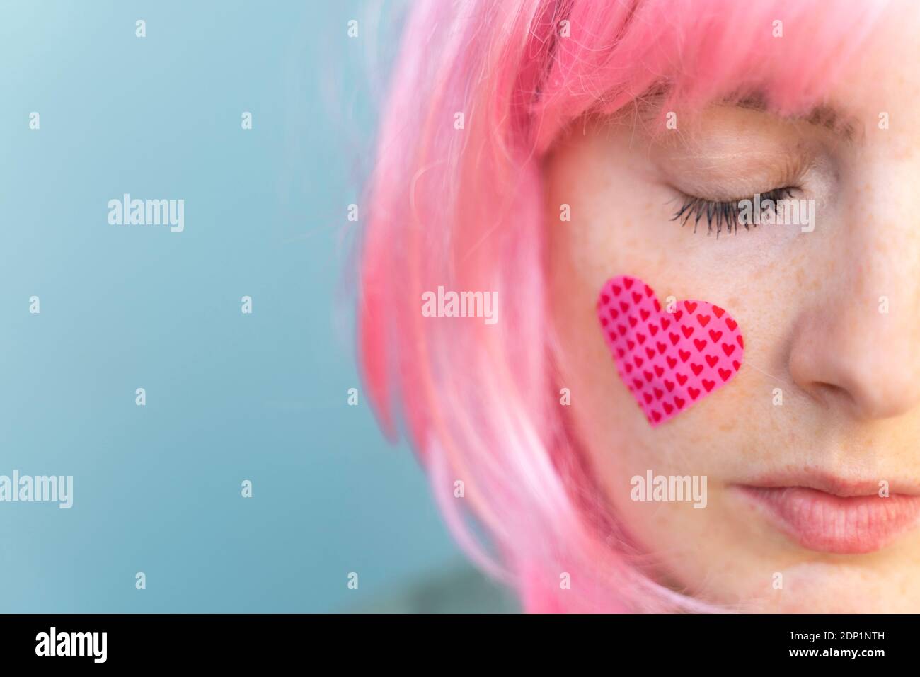 Jeune femme portant une perruque rose avec un bracelet en forme de cœur sur elle joue Banque D'Images
