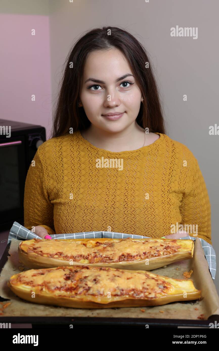 Fille dans une robe jaune tire hors du four jaune courgettes cuites sur une plaque de cuisson. Banque D'Images