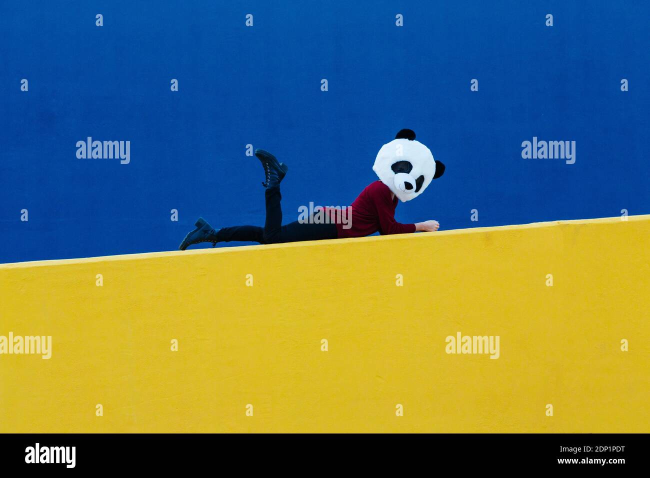 Femme portant un masque de panda tout en étant couché sur un mur jaune Banque D'Images