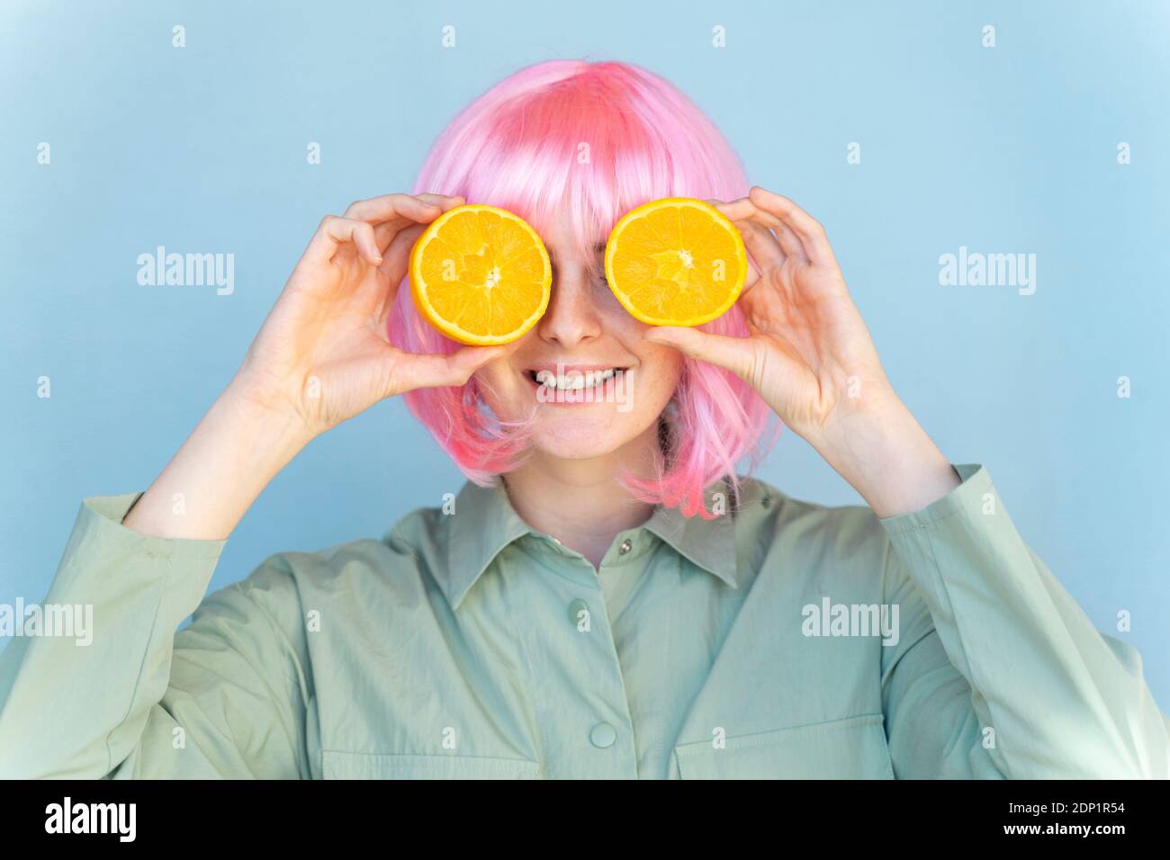 Jeune femme portant une perruque rose couvrant ses yeux avec des oranges Banque D'Images