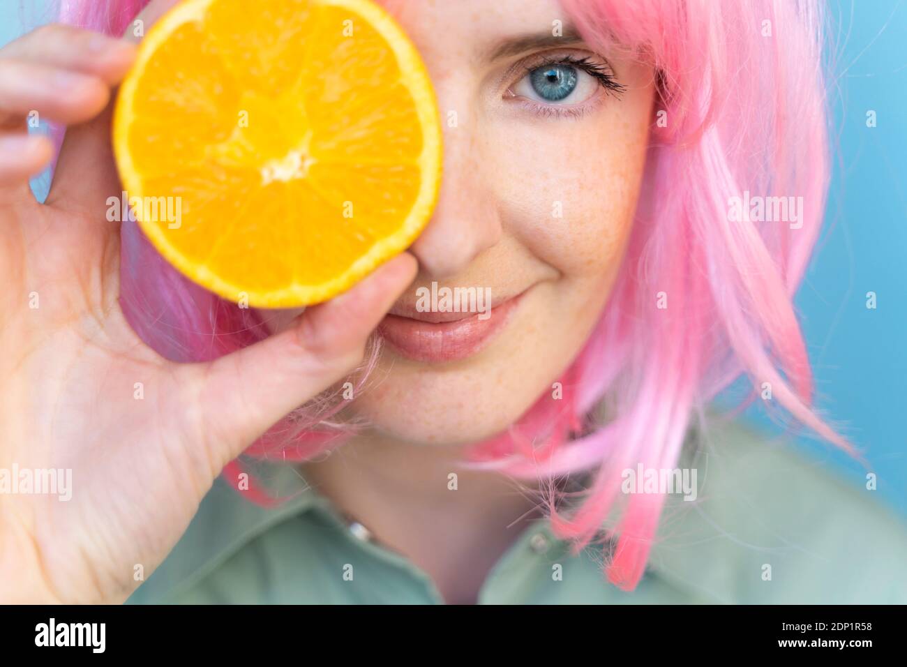 Jeune femme portant une perruque rose couvrant son œil avec un orange Banque D'Images
