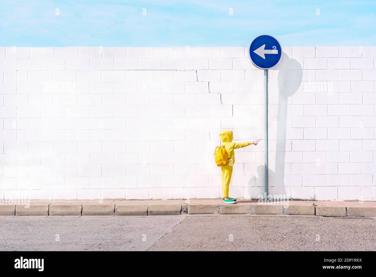 Fille avec son jouet sur un panneau de signalisation, direction à gauche devant un mur blanc Banque D'Images