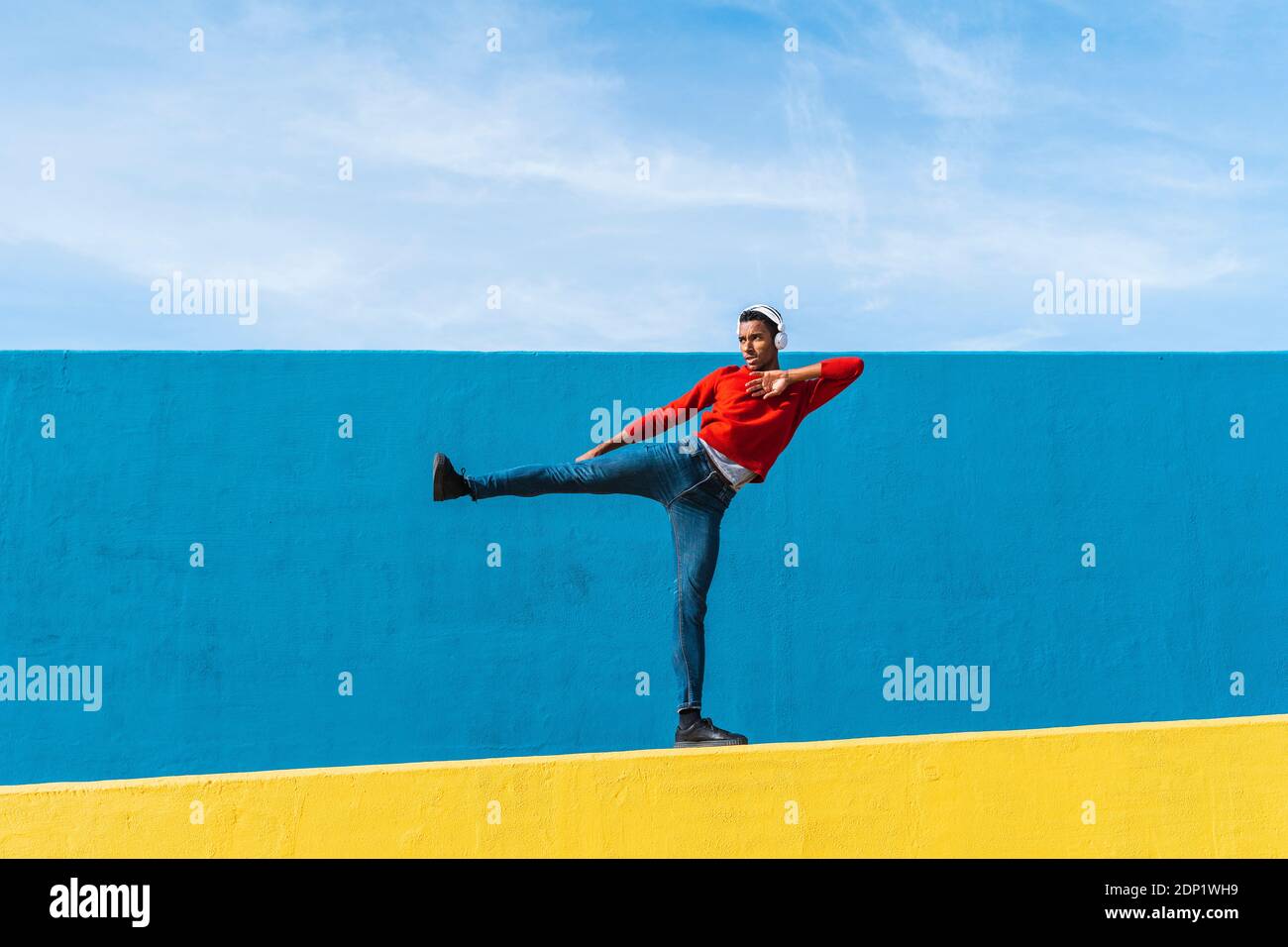 Jeune homme avec des écouteurs, l'écoute de la musique, de la danse sur le mur jaune Banque D'Images
