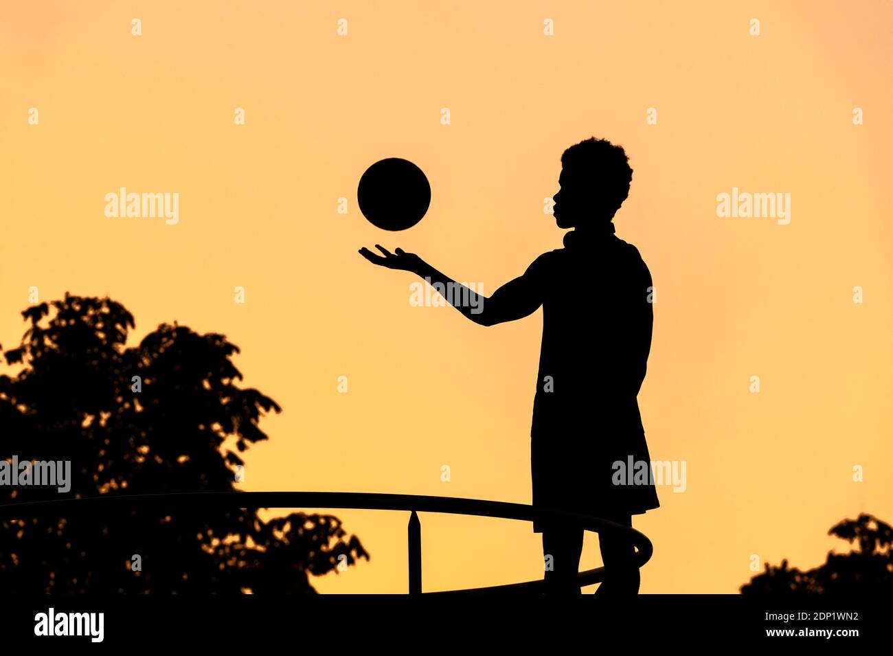 Silhouette de jeune homme avec basket-ball au coucher du soleil Banque D'Images