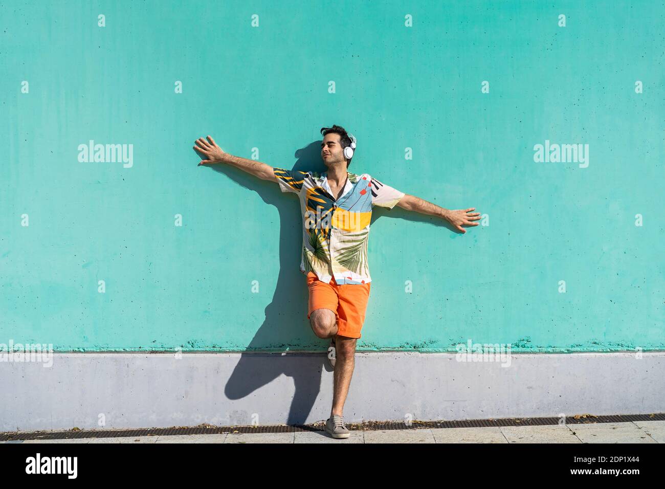 Cool homme debout devant le mur vert, en écoutant de la musique avec des écouteurs Banque D'Images