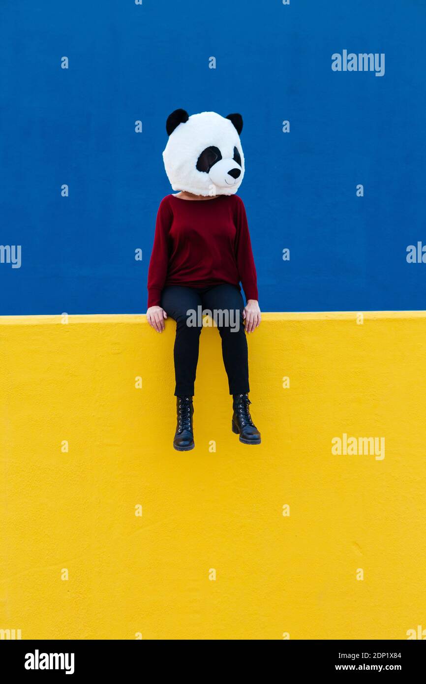 Femme dans le masque panda assis sur le mur de retenue jaune Banque D'Images