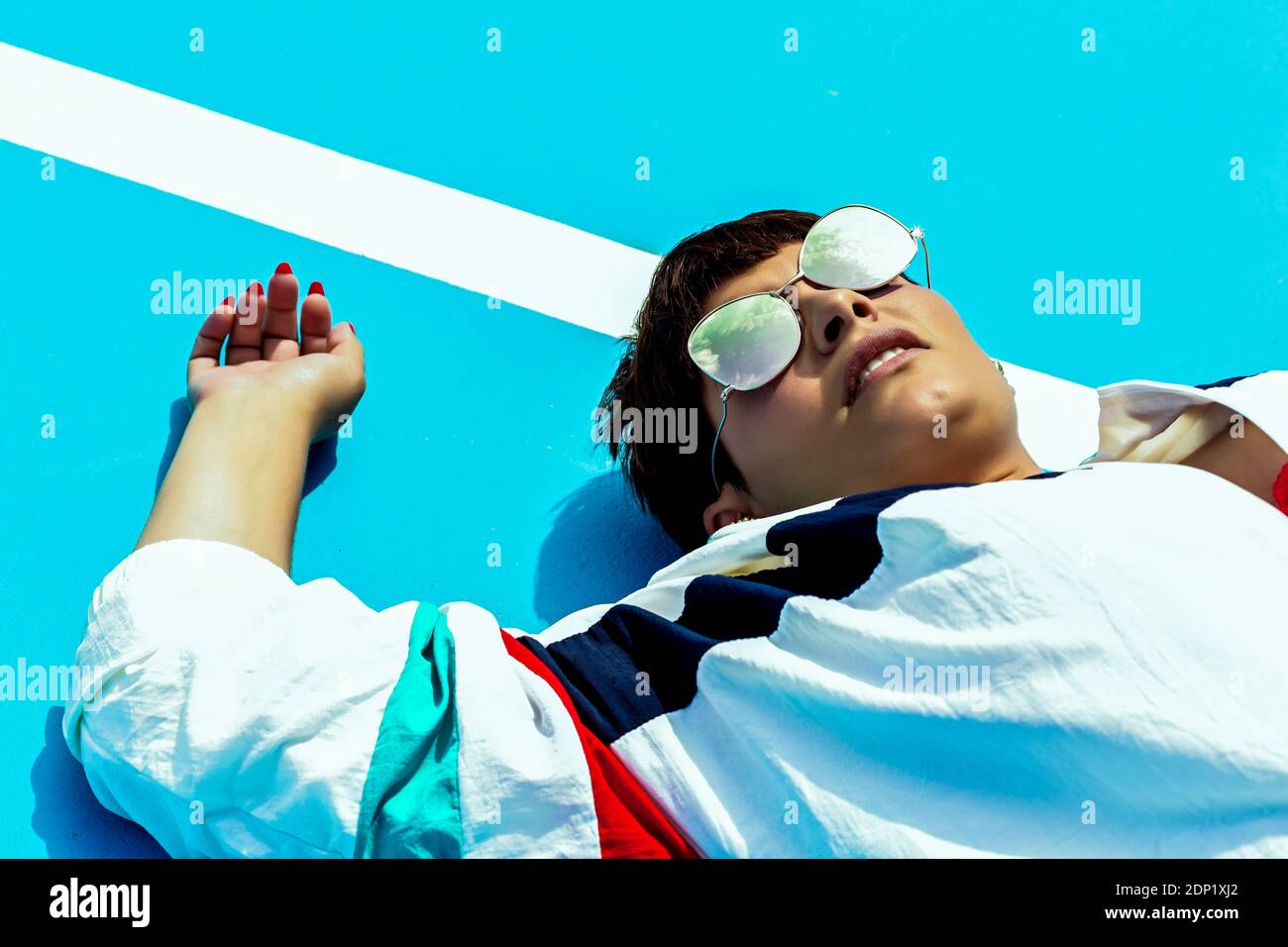 Portrait d'une femme portant des lunettes de soleil à miroir et allongé sur le sol Banque D'Images