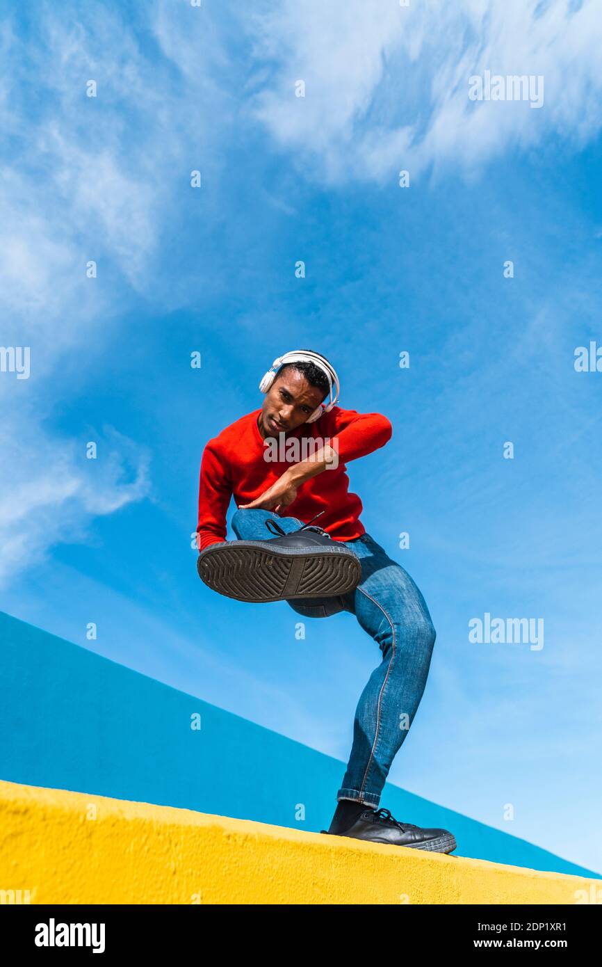 Jeune homme avec des écouteurs, l'écoute de la musique, de la danse sur le mur jaune Banque D'Images