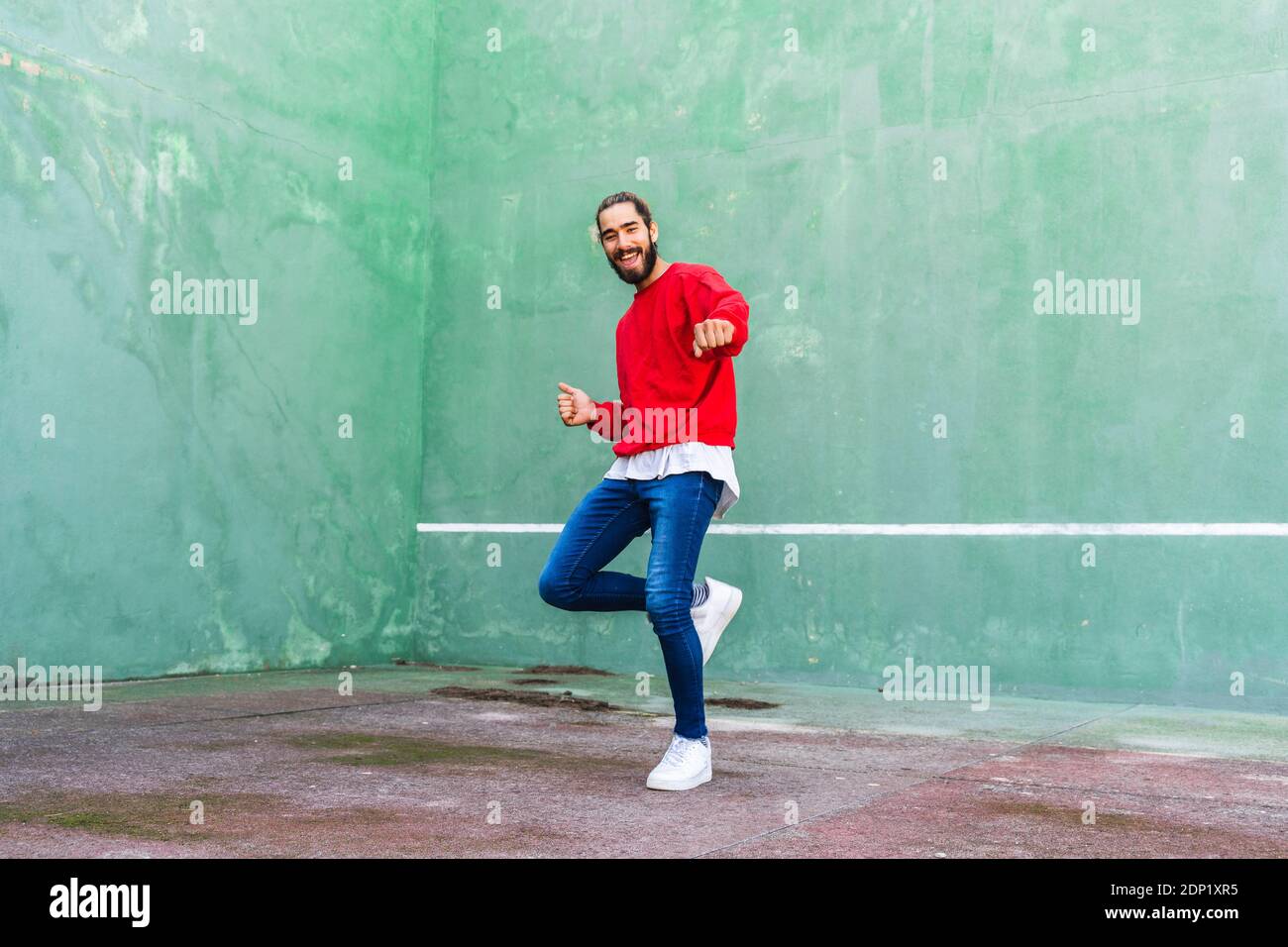 Portrait de jeune homme barbu dansant devant le mur vert Banque D'Images