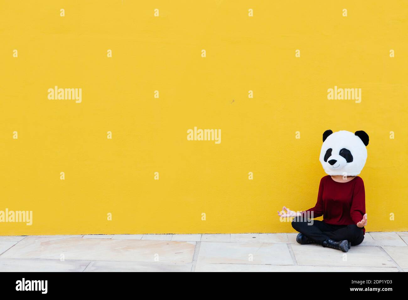 Femme portant un masque de panda tout en étant assise en position de lotus contre mur jaune Banque D'Images