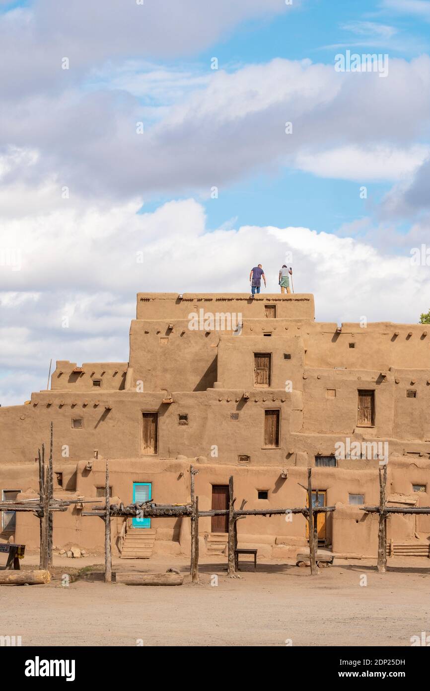 Hommes nettoyant le toit de maisons en briques de boue adobe dans le village amérindien historique de Taos Pueblo, Nouveau Mexique, États-Unis. Un site classé au patrimoine mondial de l'UNESCO. Banque D'Images