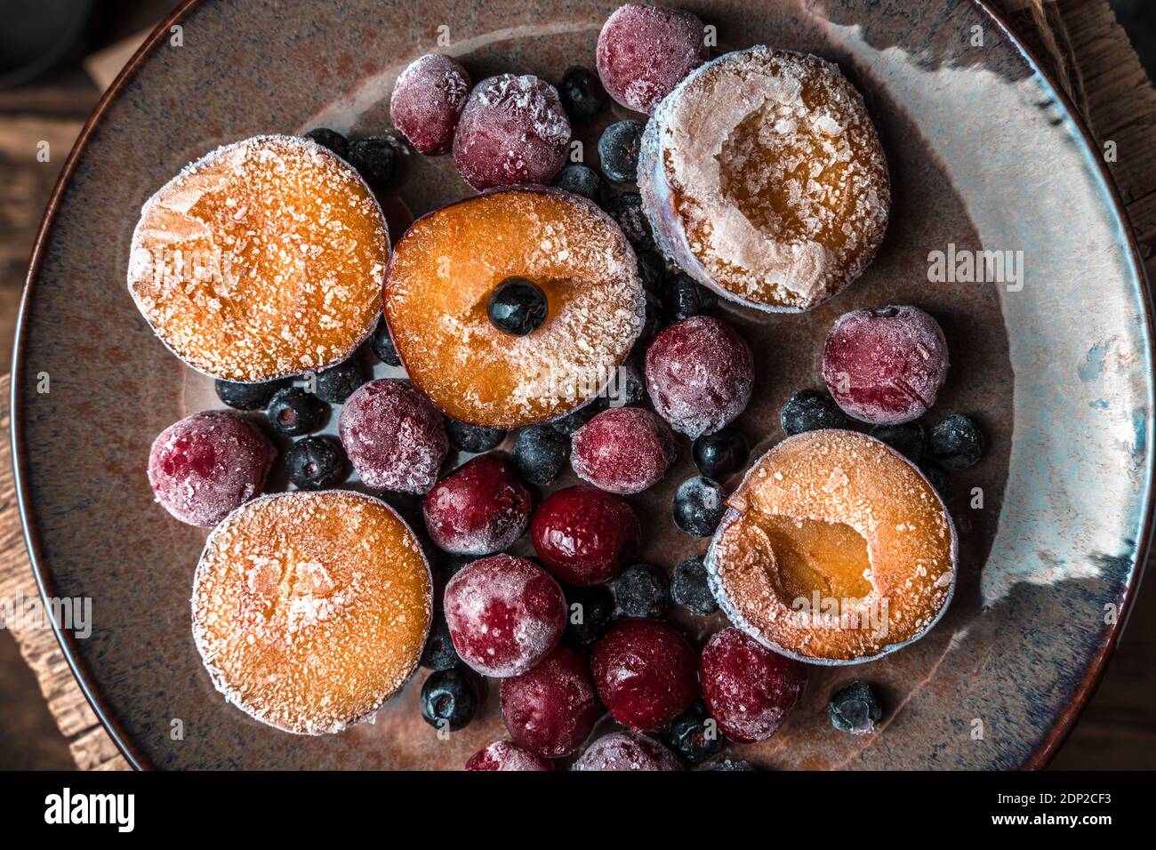 Baies, prunes et cerises congelées dans une assiette brune sur fond de bois. Banque D'Images