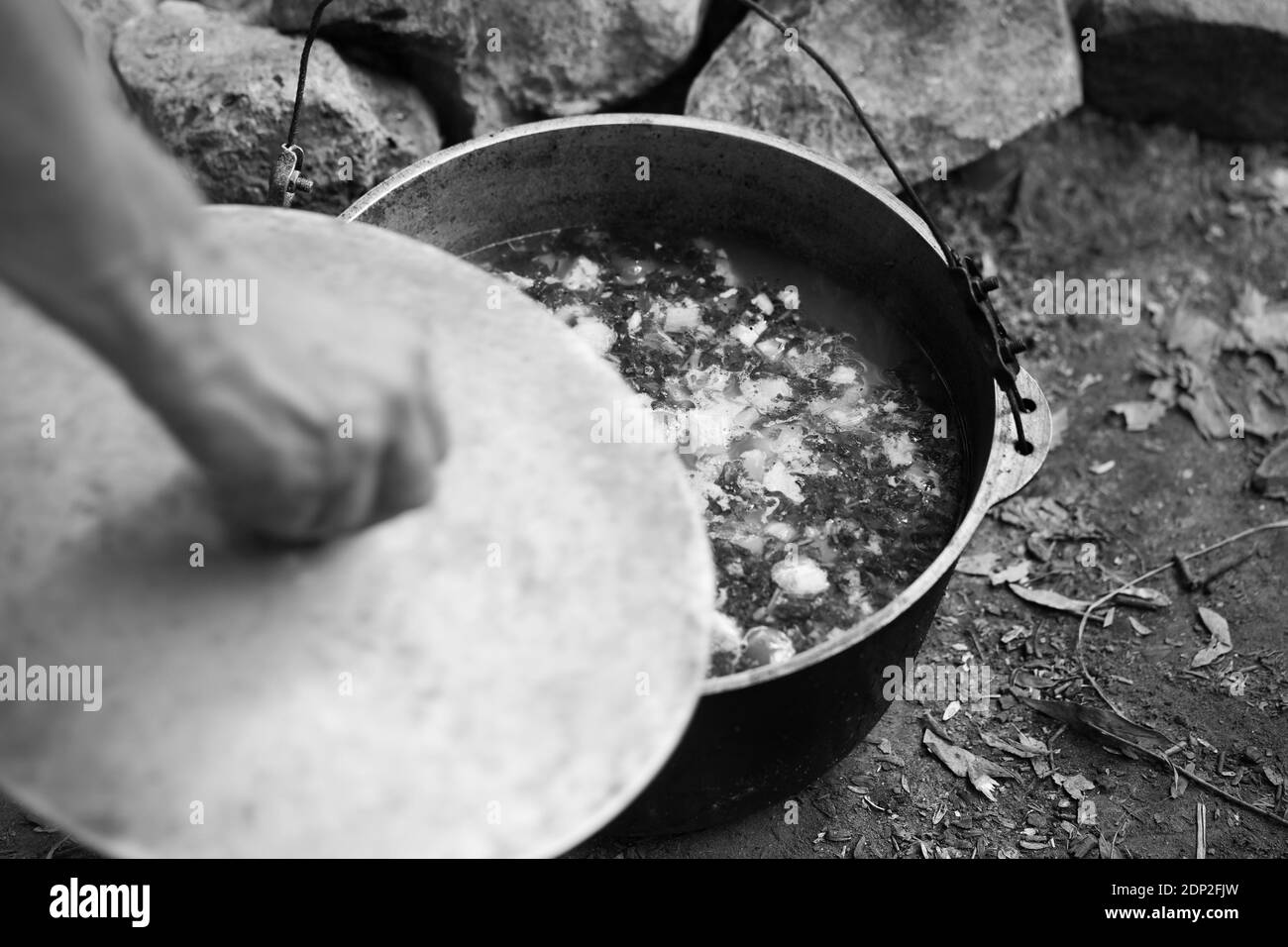 Soupe chaude fraîchement cuite dans le vieux grand chou-fleur de sucette sur le feu de camp et homme main avec couvercle de pot. Cuisine de camping en plein air. Mise au point sélective. Noir et blanc Banque D'Images