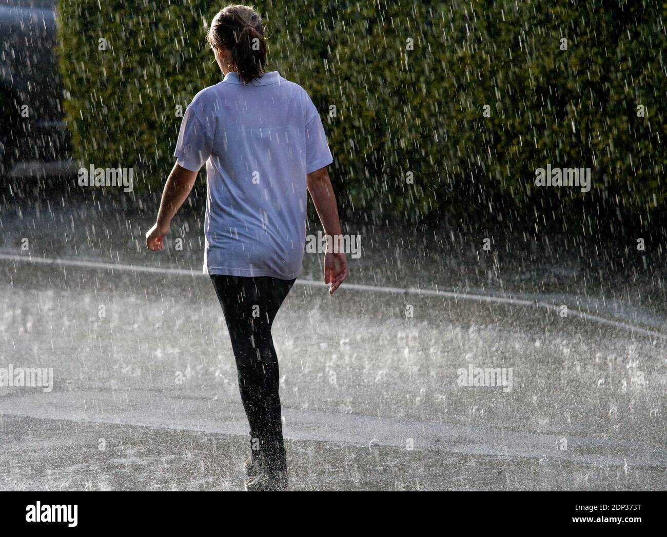 Femelle marchant dans un déversage torrentiel et trempé. Un été britannique. Des raindrops dansent du sol Banque D'Images