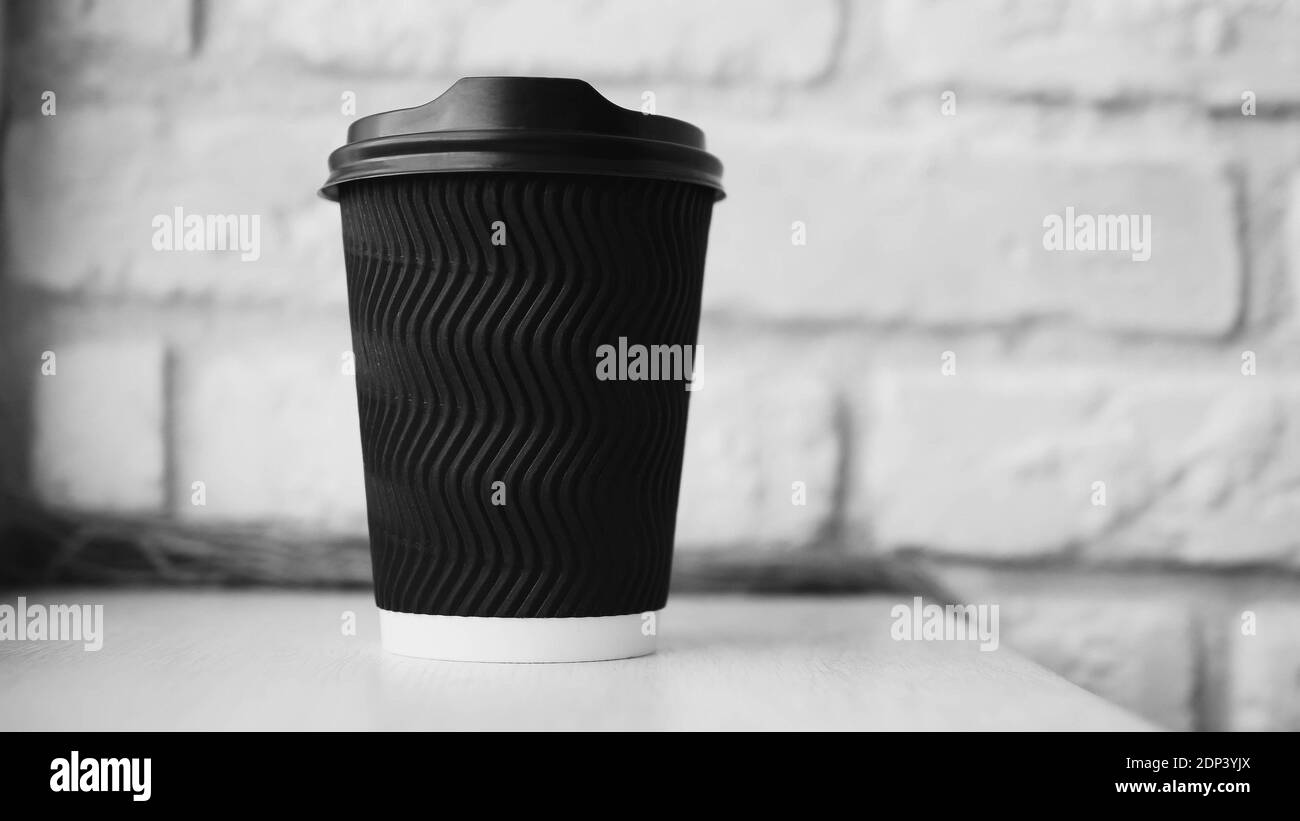 Verre à café en plastique, texture ondulée, sur le fond d'un mur de briques, café noir, cappuccino, boisson aromatique dans un verre, gros plan. Banque D'Images