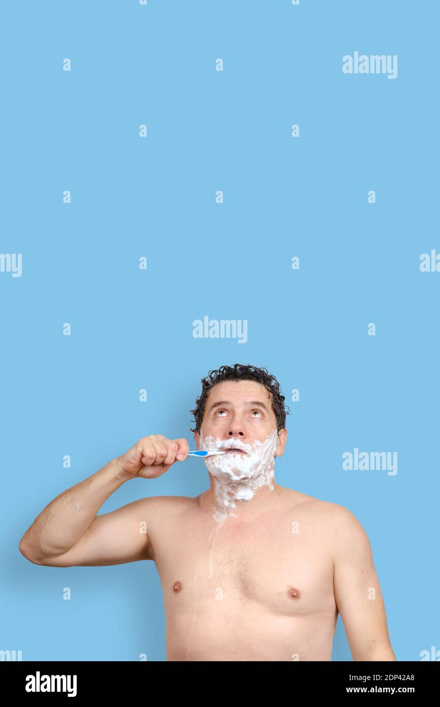 blanc homme tient une brosse à dents, se raser et regarde sur fond bleu Banque D'Images