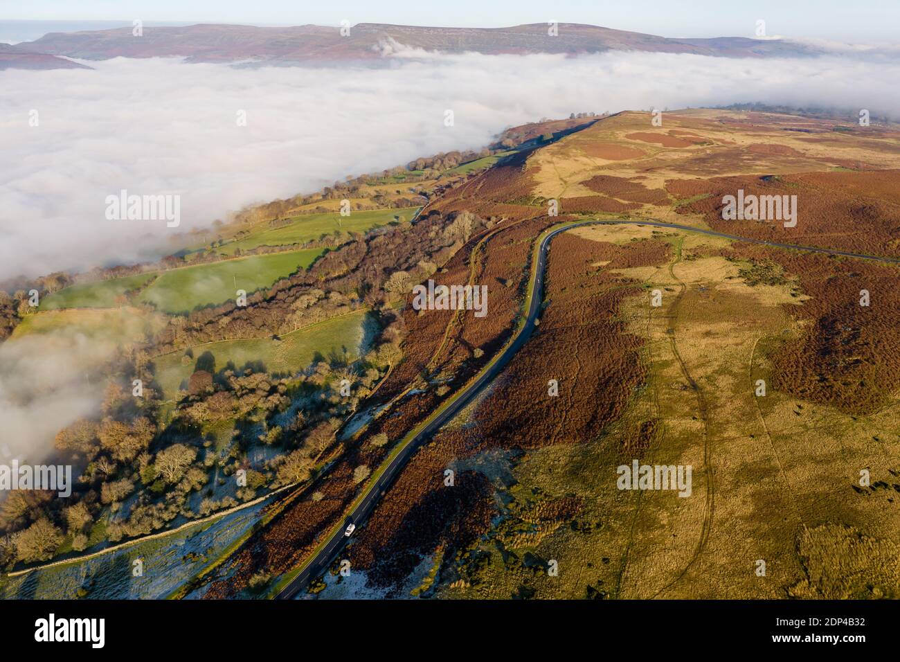 Vue aérienne d'une route de montagne étroite et sinueuse émergeant à travers une banque de brouillard et de nuages bas par temps froid et gelé (pays de Galles) Banque D'Images