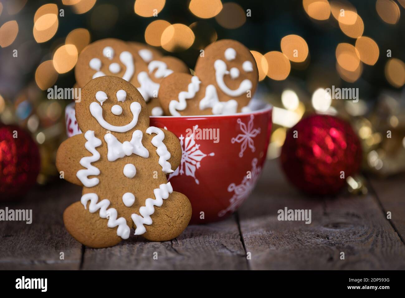 Biscuit au pain d'épice contre un bol de vacances rouge sur une table en bois. Décorations de Noël et fond doré de bokeh de vacances. Banque D'Images