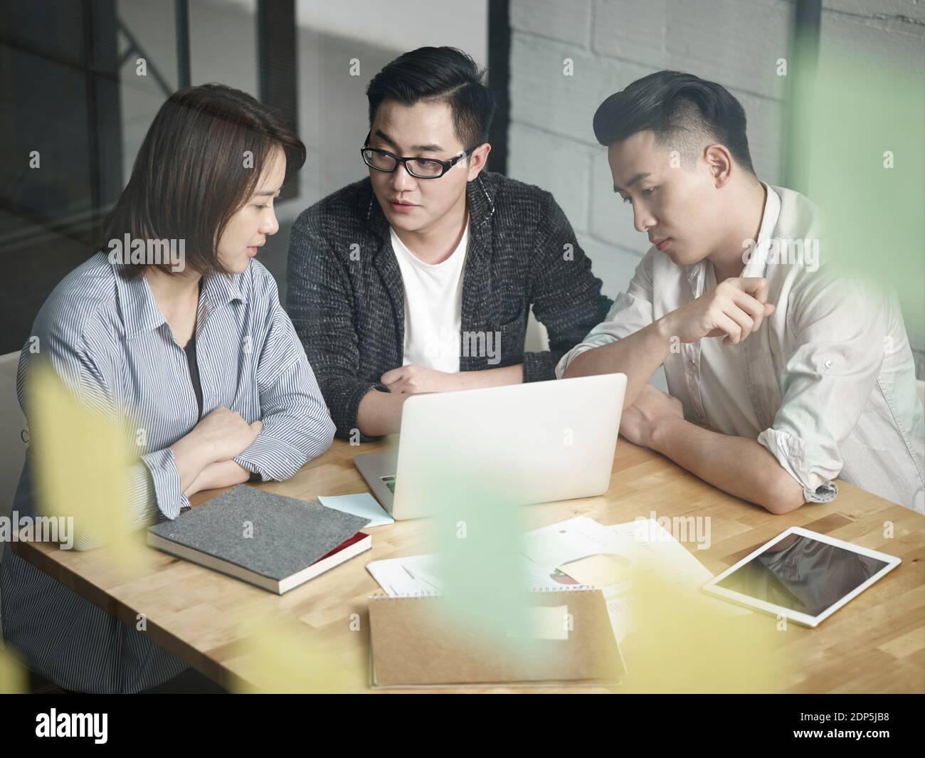 équipe de trois jeunes entrepreneurs asiatiques travaillant ensemble au bureau discuter du plan d'affaires avec un ordinateur portable Banque D'Images