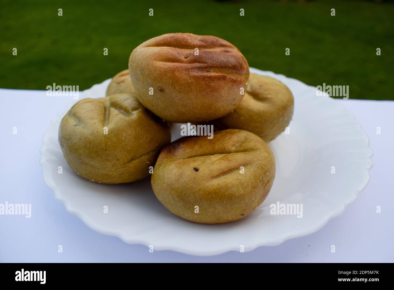 Gros plan sur le Baati ou le bati Rajasthani cuisine indienne plat une boulettes de farine de blé servi sur une assiette blanche avec pelouse fond extérieur de la loi du jardin Banque D'Images