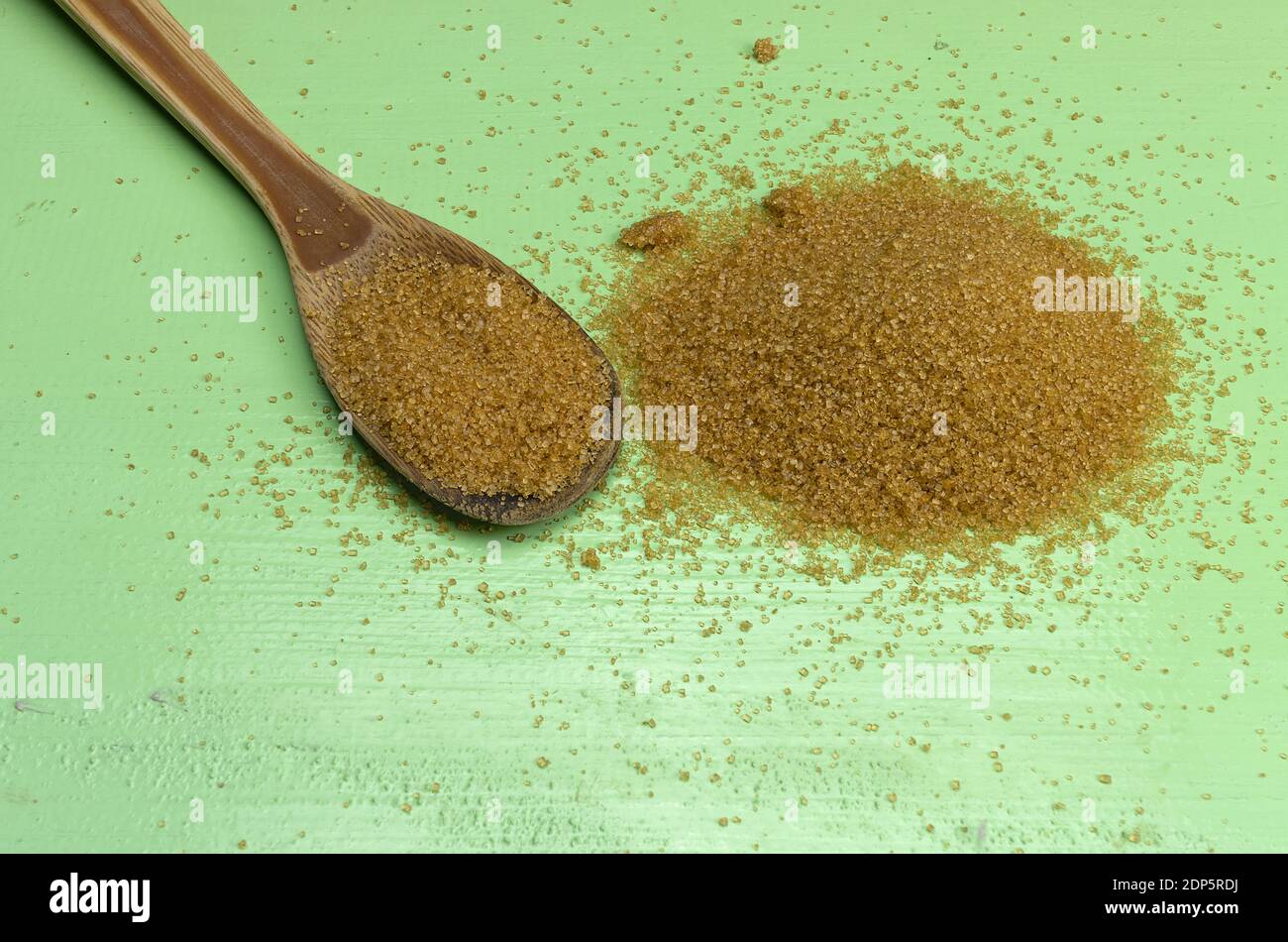 Un tas de sucre de canne brun et une cuillère en bois sur fond vert Banque D'Images