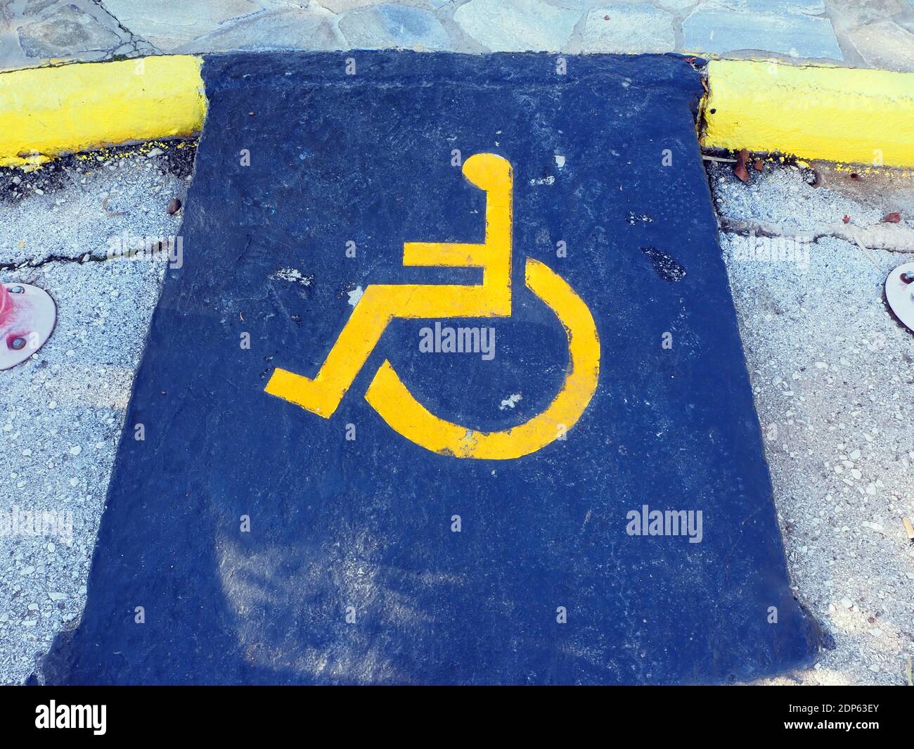 Panneau jaune pour personnes handicapées marquant un espace dans un parking, sur fond bleu dans une marina en Grèce Banque D'Images