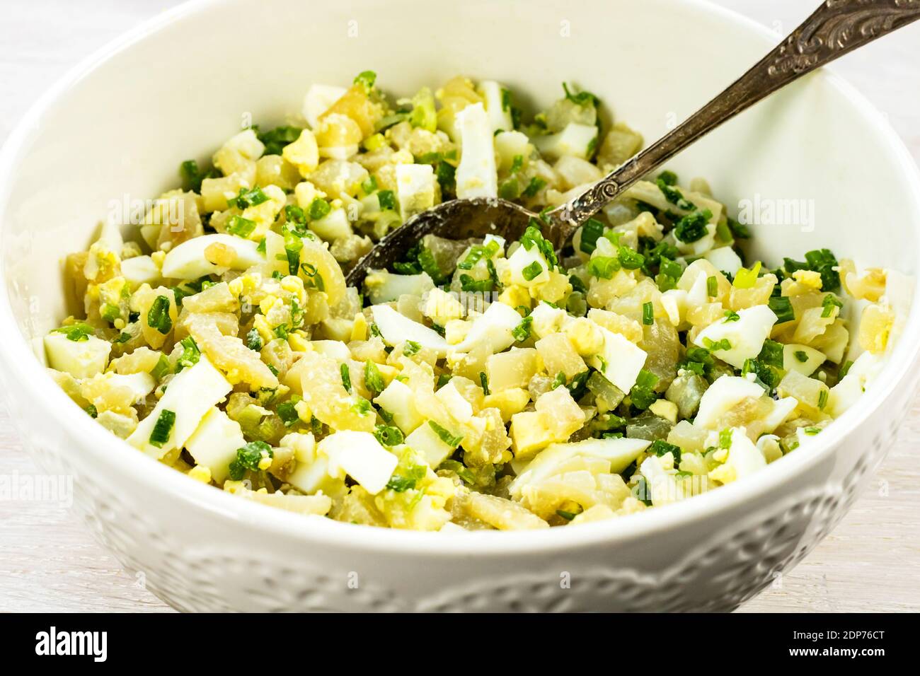 Salade de calamars, œuf, oignon vert dans un bol blanc avec une cuillère Banque D'Images