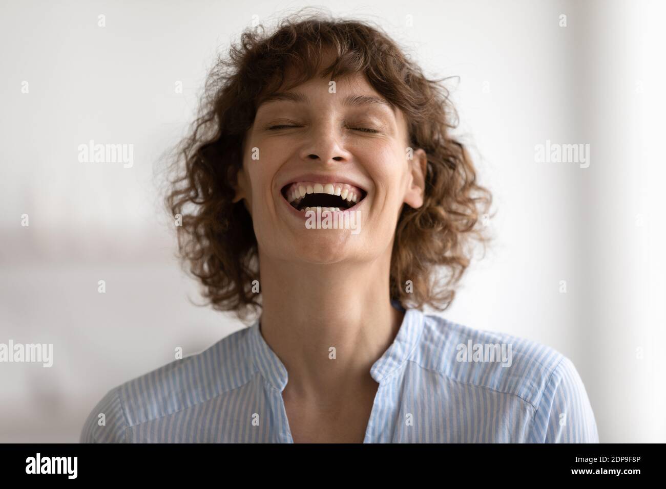 Insouciante positive jeune femme riant à haute voix avec les yeux fermés Banque D'Images