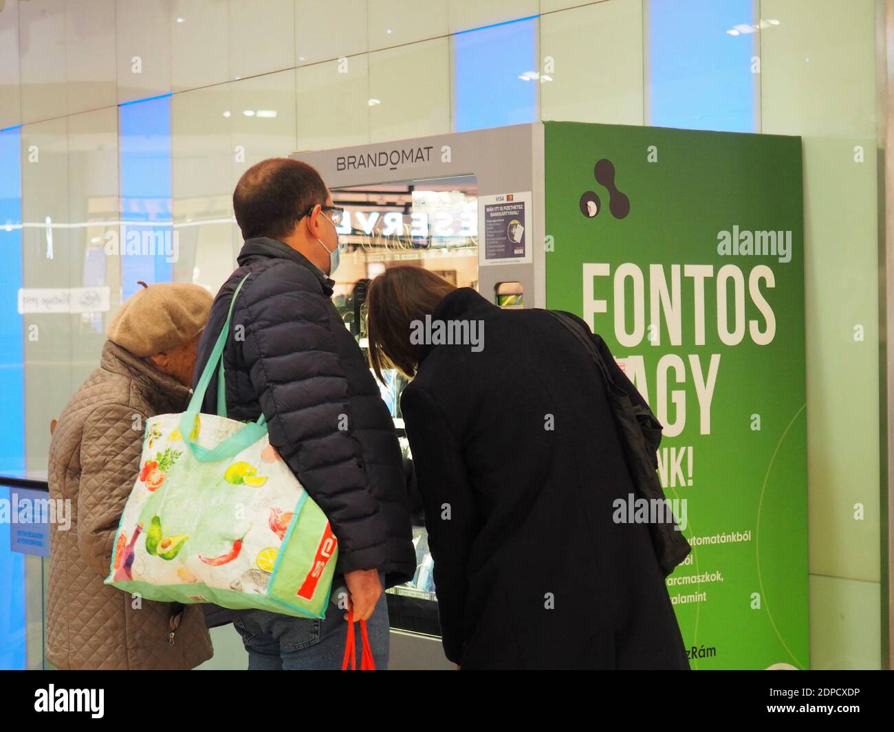 Budapest, Hongrie - 20 novembre 2020 : une femme âgée et un couple d'âge moyen regardant un distributeur de masques dans un grand centre commercial Banque D'Images