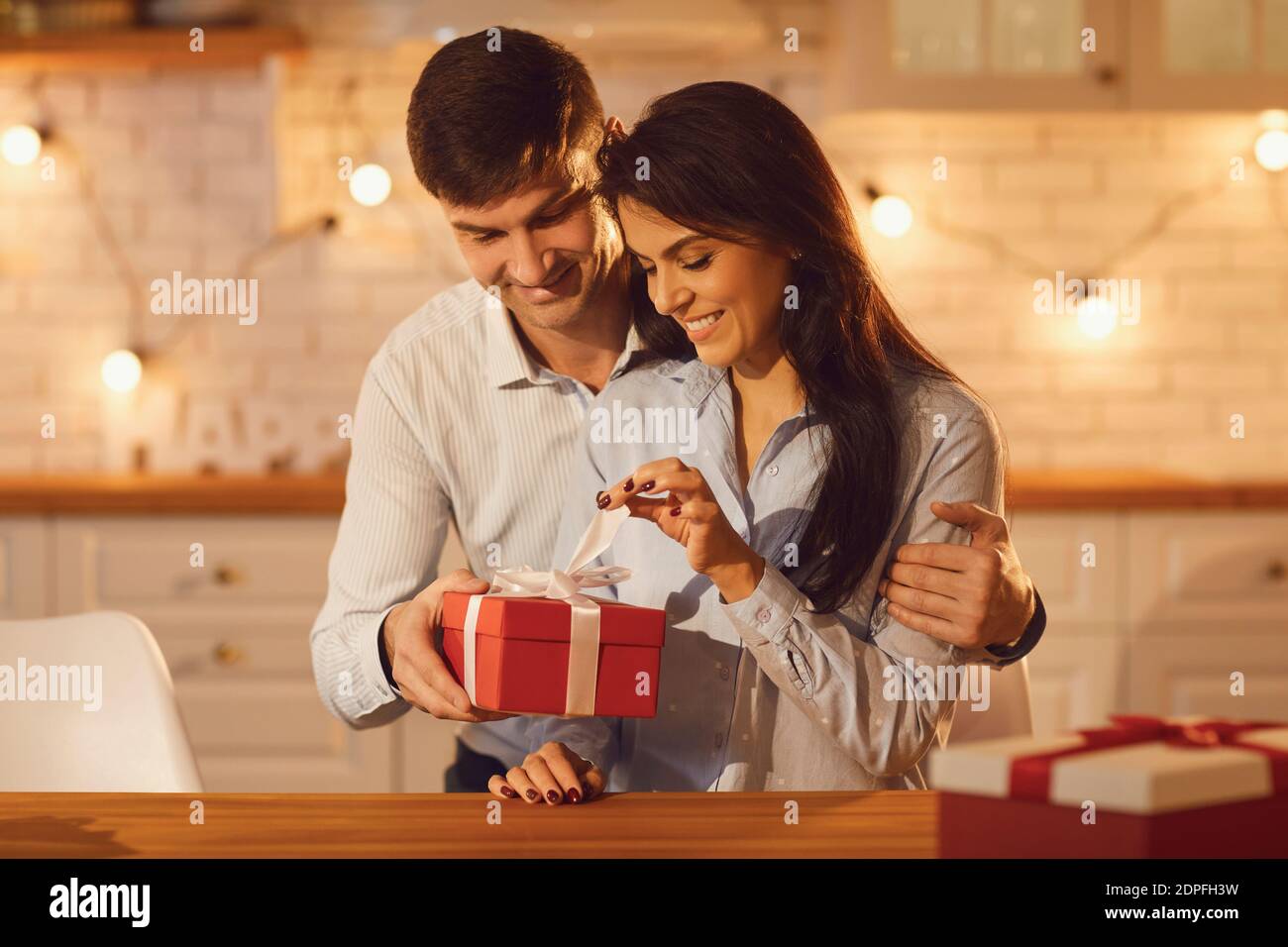 Jeune femme brune heureuse déballant le cadeau de vacances de son sourire petit ami Banque D'Images