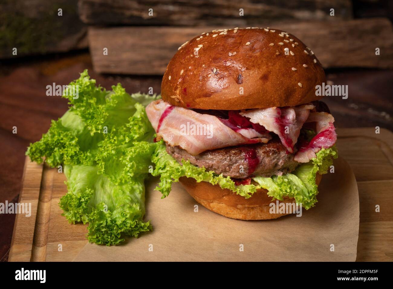 Hamburger de bœuf artisanal frais avec tranches de bacon frites et sauce aux cerises, laitue fraîche à côté. Concept de restaurant. Concept de cuisine de rue Banque D'Images