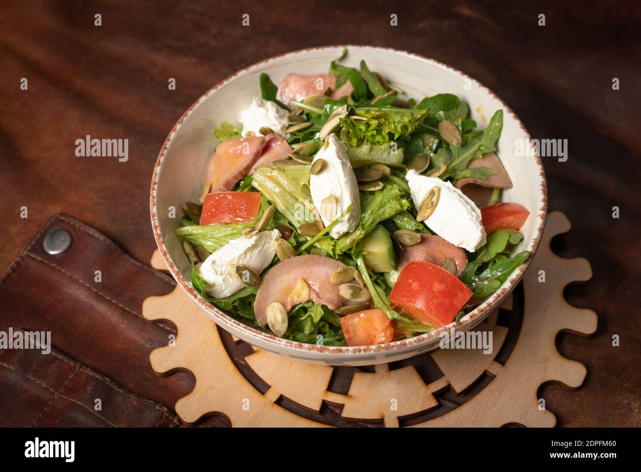 Bol de salade de légumes frais avec des tranches de saumon, fromage mozzarella sur une table recouverte d'un chiffon en cuir et d'un détail décoratif d'un Banque D'Images