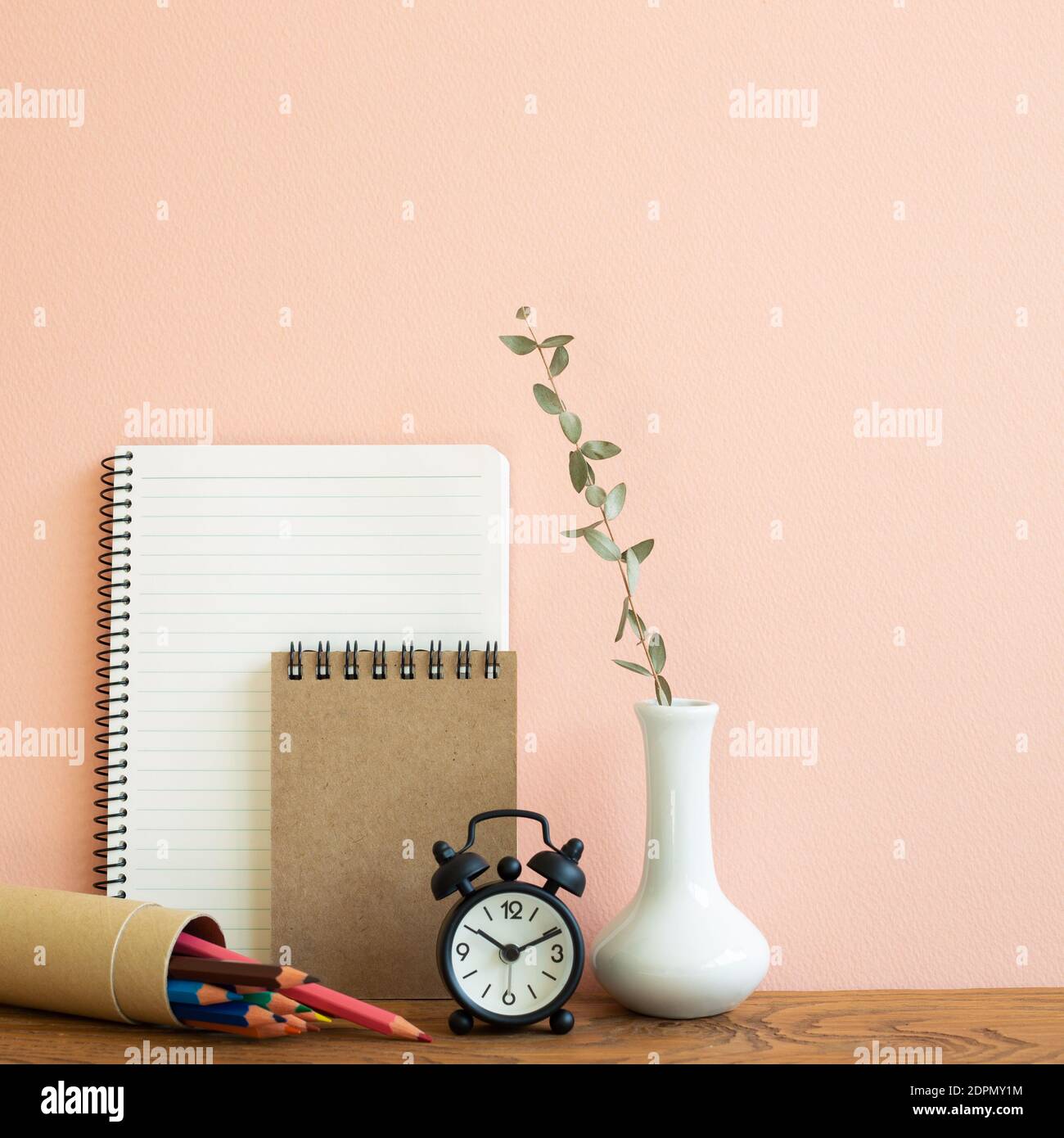 Carnet, horloge, crayons avec vase d'eucalyptus sur table en bois. Fond rose. Lieu de travail et d'étude Banque D'Images