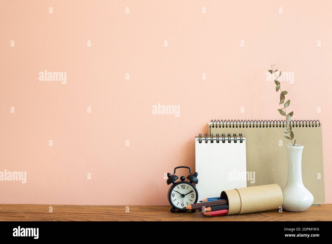 Carnet, horloge, crayons avec vase d'eucalyptus sur table en bois. Fond rose. Lieu de travail et d'étude Banque D'Images