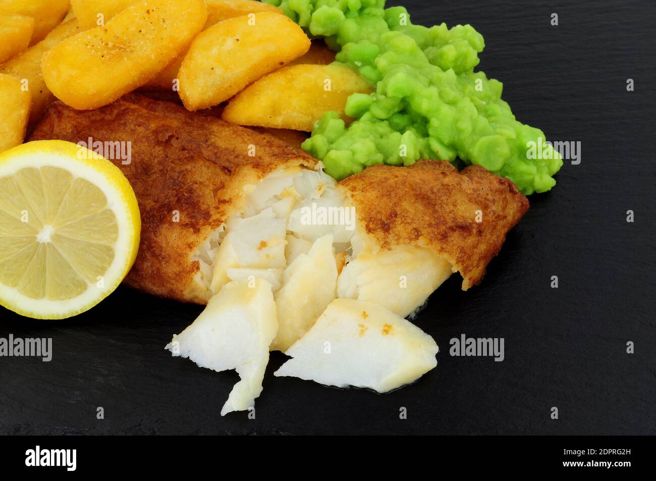Filet de morue pané avec grosses frites et petits pois molles sur fond de pierre d'ardoise Banque D'Images