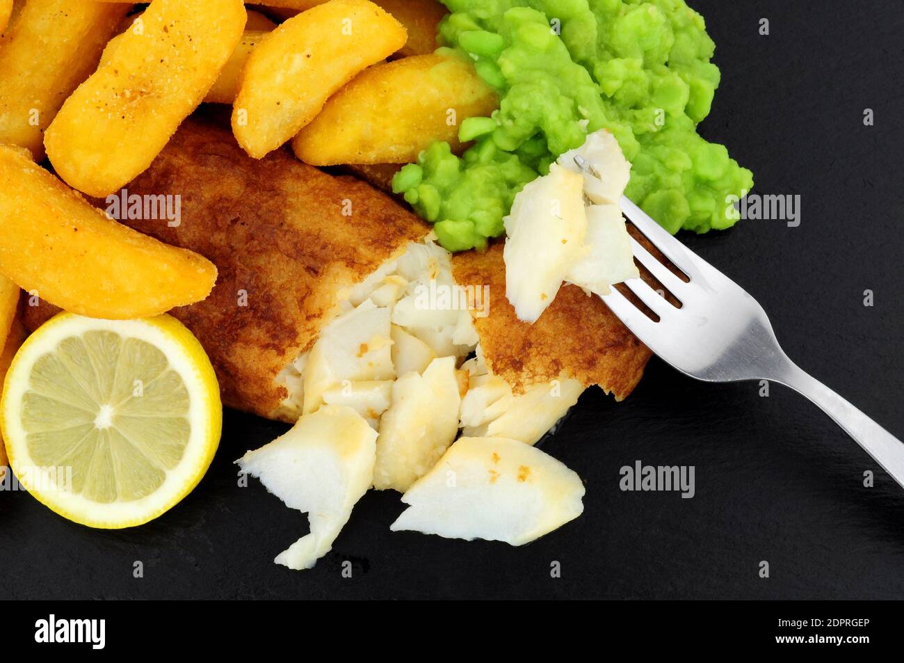 Filet de morue pané avec grosses frites et petits pois molles sur fond de pierre d'ardoise Banque D'Images