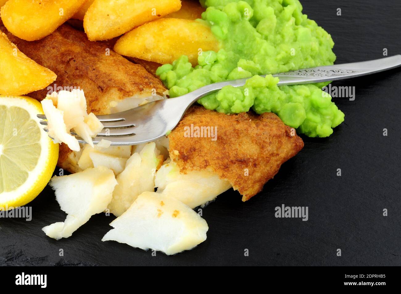 Filet de morue pané avec grosses frites et petits pois molles sur fond de pierre d'ardoise Banque D'Images