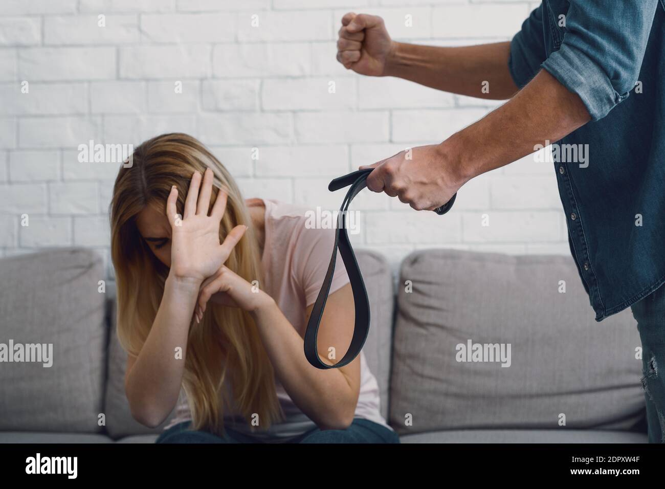 Menaces et violence physique. L'homme en colère menace avec le poing et la ceinture à la femme effrayée Banque D'Images