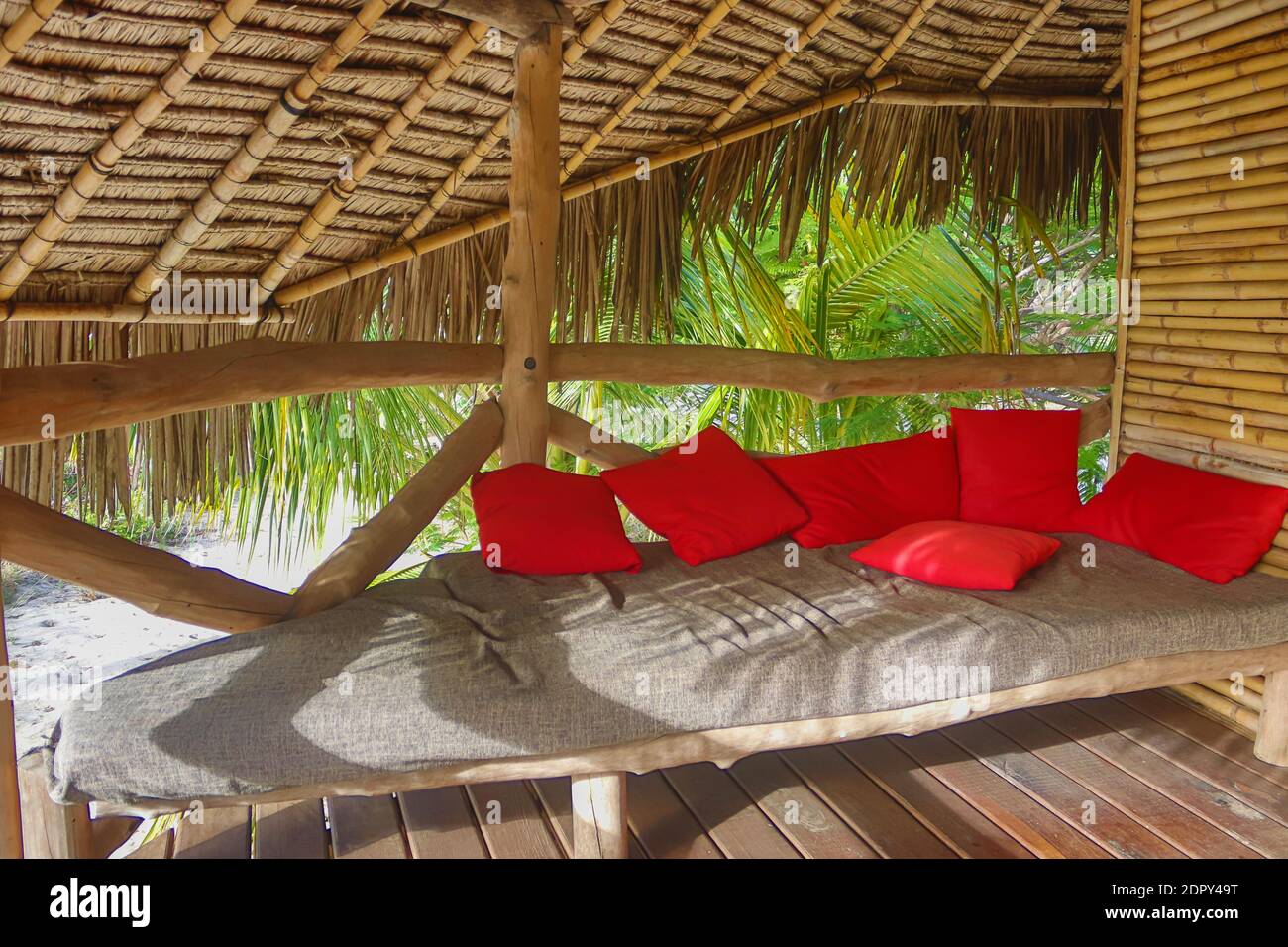 Maison écologique, la villa Jungle en bambou et matériaux locaux, chaises en bois confortables et table massive placée sur le balcon avec des oreillers rouges Banque D'Images