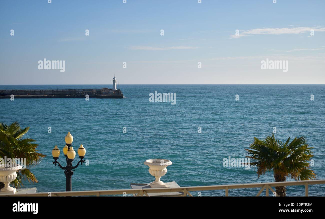 Mer ensoleillée avec lanterne et phare. Feuilles de palmier vertes. Vacances d'été. Le soleil bleu brille. Banque D'Images